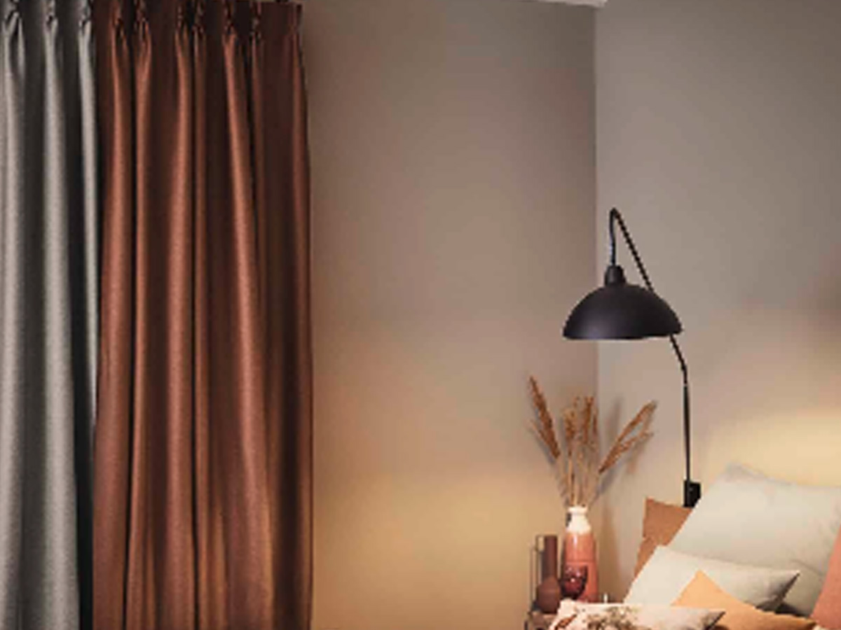 Schlafzimmer in sanften herbstlichen Tönen in Beige und Terrakotta. Links verdecken ein grauer und rostroter Thermovorhang das Fenster.