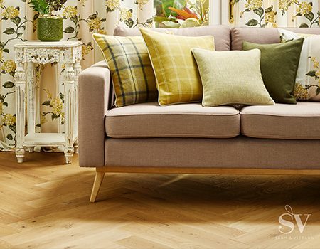 Ein moderes beiges Sofoa mit grünen Zierkissen.