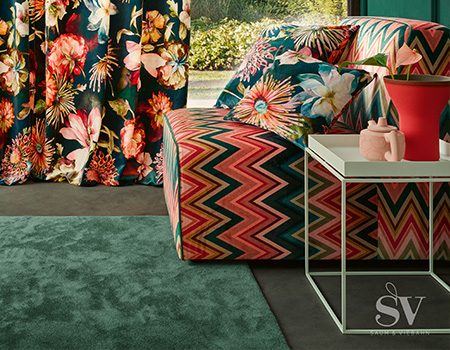 Ein bunt gemustertes Sofa- Links eine dazu passendende florale Gardine.