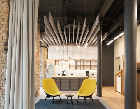 2 gelbe Sitzmöbel. Davor ein grauer Vorhang links. Oben hängend von der Decke: graue Akustikelemente. Foto: Reference – AOK Teamspace Berlin – Acoustic – 03 Photo: Peter Margis
